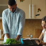 Attractive couple in the kitchen early morning. Beautiful girl chatting phone while her boyfriend cooking breakfast at home
