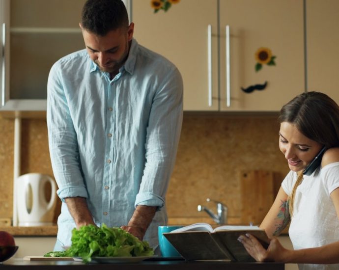 Attractive couple in the kitchen early morning. Beautiful girl chatting phone while her boyfriend cooking breakfast at home